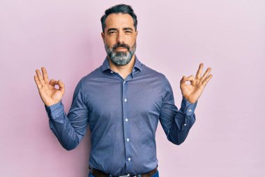 Sakallı, gri saçlı, iş kıyafetleri giyen, gözleri kapalı gülümseyen, parmaklarıyla meditasyon yapan orta yaşlı bir adam. yoga konsepti. 