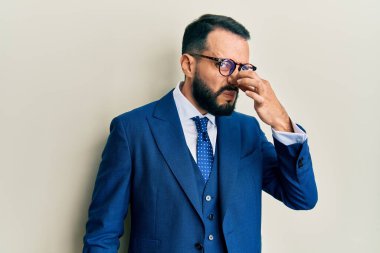 Sakallı, takım elbiseli ve kravatlı genç adam pis ve iğrenç bir koku alıyor. Nefesini burnu havada tutuyor. Kötü kokuyor. 