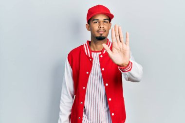 Beyzbol forması giyen genç Afro-Amerikan bir adam avuç içiyle şarkı söylemeyi kesiyor. Yüzünde olumsuz ve ciddi bir jest olan uyarı ifadesi. 