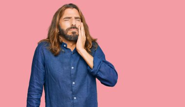 Uzun saçlı ve sakallı çekici bir adam diş ağrısı ya da diş ağrısı yüzünden ağıza dokunuyor. dişçi 