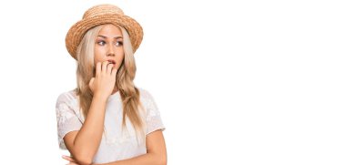 Yazlık şapkalı genç sarışın kız gergin ve gergin görünüyor. Ağzı tırnak yiyen ellerle. anksiyete. 