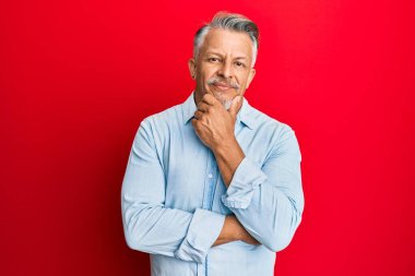 Orta yaşlı, gri saçlı, günlük kıyafetler giyen, kameraya kendinden emin, kolları çapraz ve çenesi açık gülümseyen bir adam. Olumlu düşünmek. 