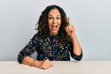 Gündelik giysiler giymiş orta yaşlı güzel bir kadın masaya oturmuş başarılı bir fikirle işaret ediyor. Heyecanlı ve mutlu. Bir numara.. 