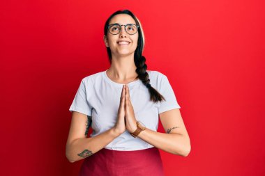 Genç İspanyol kadın profesyonel garson önlüğü giyiyor. Elleriyle yalvarıyor ve dua ediyor. Yüzünde umut ifadesi var. Yalvarıyor. 