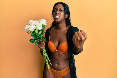 Genç Afrikalı Amerikalı kadın elinde çiçeklerle sinirli ve sinirli bir şekilde bağırıyor, öfkeyle çılgınca bağırıyor ve elini kaldırıyor. 