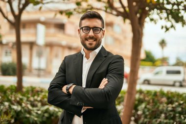 Kollarını kavuşturmuş genç İspanyol işadamı şehirde mutlu bir şekilde gülümsüyor..