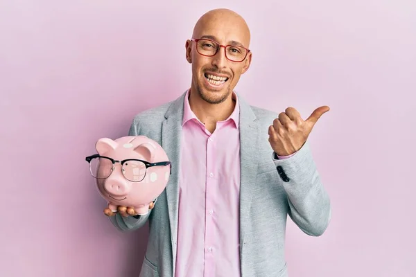 Bald Man Beard Holding Piggy Bank Glasses Pointing Thumb Side — Foto Stock