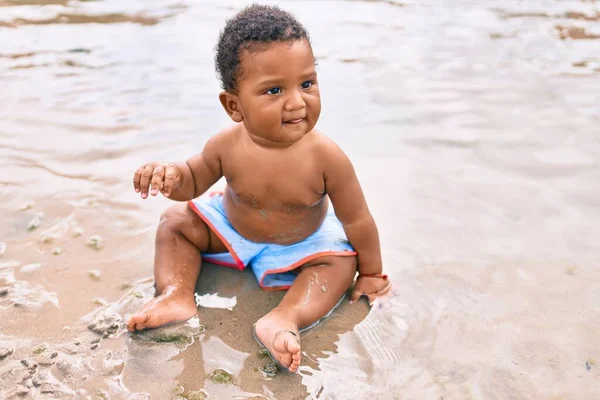 愛らしいアフリカ系アメリカ人の幼児がビーチに座っています — ストック写真