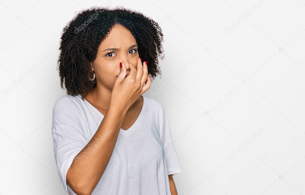 Young african american girl wearing casual clothes smelling something stinky and disgusting, intolerable smell, holding breath with fingers on nose. bad smell 