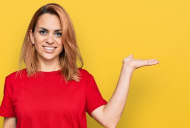 İspanyol asıllı genç bir kadın, günlük kırmızı tişört giyiyor. Gülümsüyor, gülümsüyor ve avuç içi kameraya bakıyor.. 