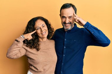 Orta yaşlı İspanyol çift gündelik kıyafetler giyip gülümsüyor ve tek parmağıyla kafasını işaret ediyor. Harika bir fikir ya da düşünce, iyi bir hafıza. 