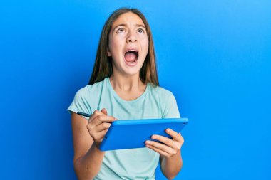 Güzel esmer küçük kız ekranda dokunmatik çizim yapıyor kızgın ve kızgın çığlıklar atıyor öfkeyle bağırıyor, öfkeyle yukarı bakıyor. 