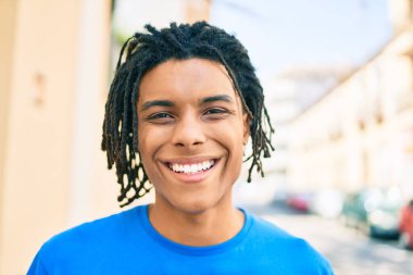 Genç Afrikalı Amerikalı adam gülümsüyor. Şehrin caddesinde kameraya bakıyor..