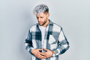 Modern boyalı saçları olan genç İspanyol bir adam elleri karnında rahat bir gömlek giyiyor çünkü hazımsızlık, acı verici bir hastalık ve kendini iyi hissetmiyor. Ağrı kavramı. 