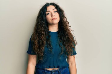 Kıvırcık saçlı, günlük kıyafetler giyen esmer bir kadın. Yüzünde ciddi bir ifadeyle rahatlamış. Basit ve doğal bir şekilde kameraya bakıyorsun.. 