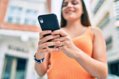 Ortadoğulu genç kız şehirde akıllı telefon kullanarak mutlu bir şekilde gülümsüyor..