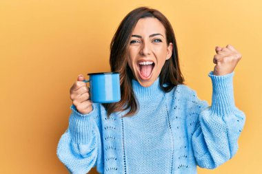 Genç esmer kadın elinde bir fincan kahveyle gururla bağırıyor, zaferi kutluyor ve kollarını kaldırarak çok heyecanlanıyor. 