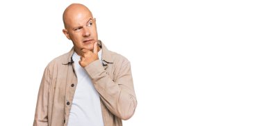 Orta yaşlı kel bir adam, elleri çenesinde gündelik giysiler giyip soru soruyor, düşünceli bir yüz ifadesi var. Düşünceli bir yüzle gülümsüyor. şüphe kavramı. 