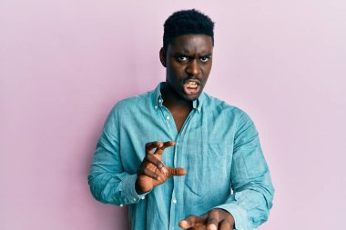 Yakışıklı, sıradan kıyafetler giyen, tiksindirici ifadeler takınan, tiksindirici, tiksindirici yüz ifadeleri olan siyahi bir adam. Eller havada. 