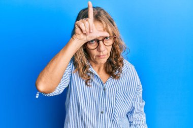 Orta yaşlı sarışın kadın günlük kıyafetler ve gözlük takıyor. Alnında parmakları olan insanlarla dalga geçiyor. Ezik hareketler yapıyor, alay ediyor ve hakaret ediyor.. 