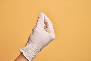 İzole edilmiş sarı arka plan üzerinde tıbbi eldiveni olan, parmak, iş ve reklamla boş alan tutan beyaz bir gencin eli.