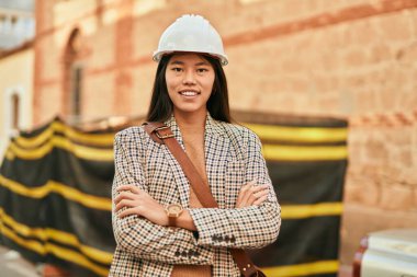 Kollarını kavuşturmuş genç Asyalı mimar şehirde mutlu bir şekilde gülümsüyor..