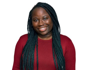 Saçları örgülü genç siyahi bir kadın pozitif ve mutlu görünüyor ve kendine güvenen bir gülümsemeyle dişlerini gösteriyor. 