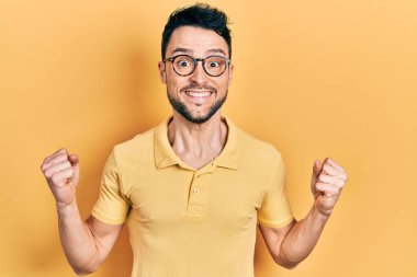 Gündelik kıyafet ve gözlük takan genç İspanyol adam kollarını kaldırıp, gözlerini açarak başarının şokunu yaşıyor ve hayrete düşüyor. Kazanan konsept. 