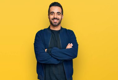 Gündelik kıyafetler giyen, kollarını kavuşturup kameraya gülümseyen genç İspanyol adam. pozitif kişi. 