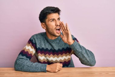 Kış süveteri giymiş genç yakışıklı adam masaya oturmuş el ele tutuşmuş bağırıyor ve çığlık çığlığa bağırıyordu. iletişim konsepti. 