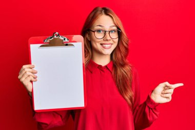 Genç kızıl saçlı kadın elinde boş alanı olan bir pano tutarken gülümsüyor mutlu bir şekilde elini ve parmağını yana uzatıyordu. 