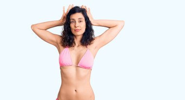 Bikini giyen, tavşan kulağı hareketi yapan genç, İspanyol bir kadın. Avuçlarıyla alaycı ve şüpheci görünüyor. Paskalya tavşanı konsepti. 