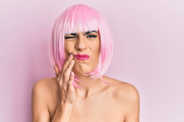 Young man wearing woman make up wearing pink wig touching mouth with hand with painful expression because of toothache or dental illness on teeth. dentist 