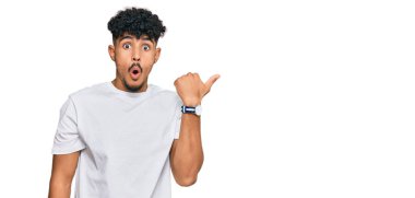 Gündelik beyaz t-shirt giyen genç Arap adam elleri yana doğru işaret ederek şaşırdı, ağzı açık hayret içinde kaldı.. 