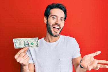 İspanyol asıllı genç adam elinde 1 dolarlık banknotla başarıyı mutlu bir gülümsemeyle kutluyor ve kazanan el kaldırıyor. 