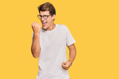 Sıradan kıyafetler ve gözlük takan yakışıklı beyaz adam kolları havada ve gözleri kapalı bir şekilde başarıyı kutluyor ve şaşırıyor. Kazanan konsept. 