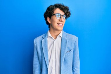 Hispanic young man wearing business jacket and glasses looking away to side with smile on face, natural expression. laughing confident. 