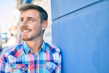 Beyaz bir adam gülümsüyor. Şehrin duvarına yaslanıyor..