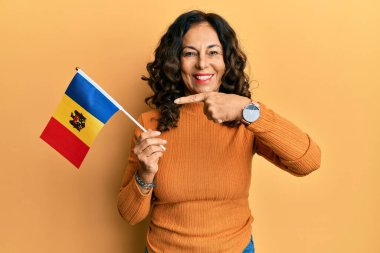 Orta yaşlı İspanyol kadın Moldova bayrağını tutarken mutlu bir şekilde el ve parmağıyla işaret ediyor. 