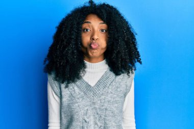 African american woman with afro hair wearing casual winter sweater puffing cheeks with funny face. mouth inflated with air, crazy expression. 