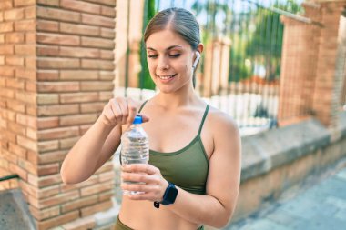 Genç sarışın sporcu şehirde bir şişe su içerek egzersiz yapıyor..