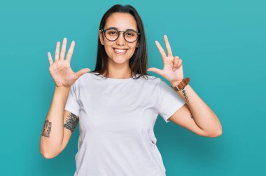 Gündelik beyaz tişört giyen genç İspanyol kadın sekiz numarayı gösterip işaret ederken kendinden emin ve mutlu gülümsüyor.. 