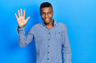 Genç Afro-Amerikalı günlük kıyafetler giymiş beş numarayı gösterip işaret ederken kendinden emin ve mutlu bir şekilde gülümsüyor.. 
