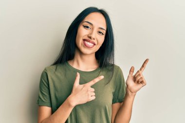 Gündelik tişört giyen genç İspanyol kız gülümseyip kameraya bakıyor ve iki eliyle ve parmaklarıyla kenarı işaret ediyor.. 