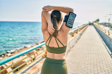 Genç sarışın sporcu kadın arka planda spor giysileri giyerek gezinti alanında geriniyor..