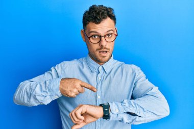 Gündelik kıyafet ve gözlük takan genç İspanyol adam saati, sabırsızlığı ve gecikmeye kızmayı işaret ediyor. 