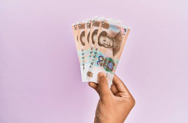 Hispanik el 20 Yuan 'lık Çin banknotunu soyutlanmış pembe arka planda tutuyor.
