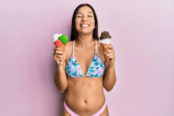 ビキニを着た若いラテン系の女性が 楽しそうに冷たい笑顔で笑顔でアイスクリームを抱えています 歯を見せて — ストック写真