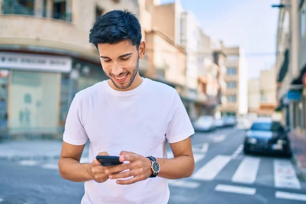 若いラテン語の男笑顔幸せな使用してスマートフォン街を歩く — ストック写真