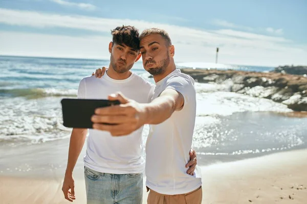 在海滩上 一对年轻的同性恋夫妇一边笑着一边用智能手机自拍 — 图库照片